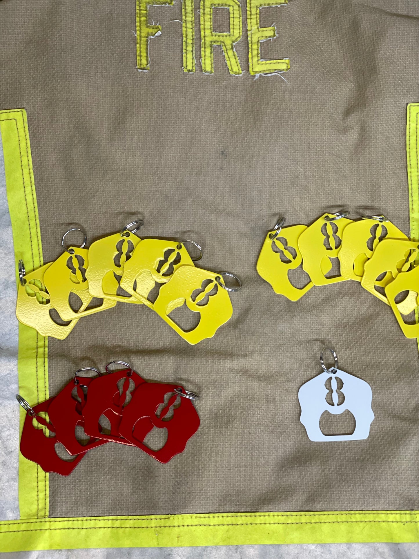 "Firefighter helmet shield keychains with red, white, and yellow powder coat finishes, personalized unit number, and built-in bottle openers, custom firefighter accessories for keys or gear."