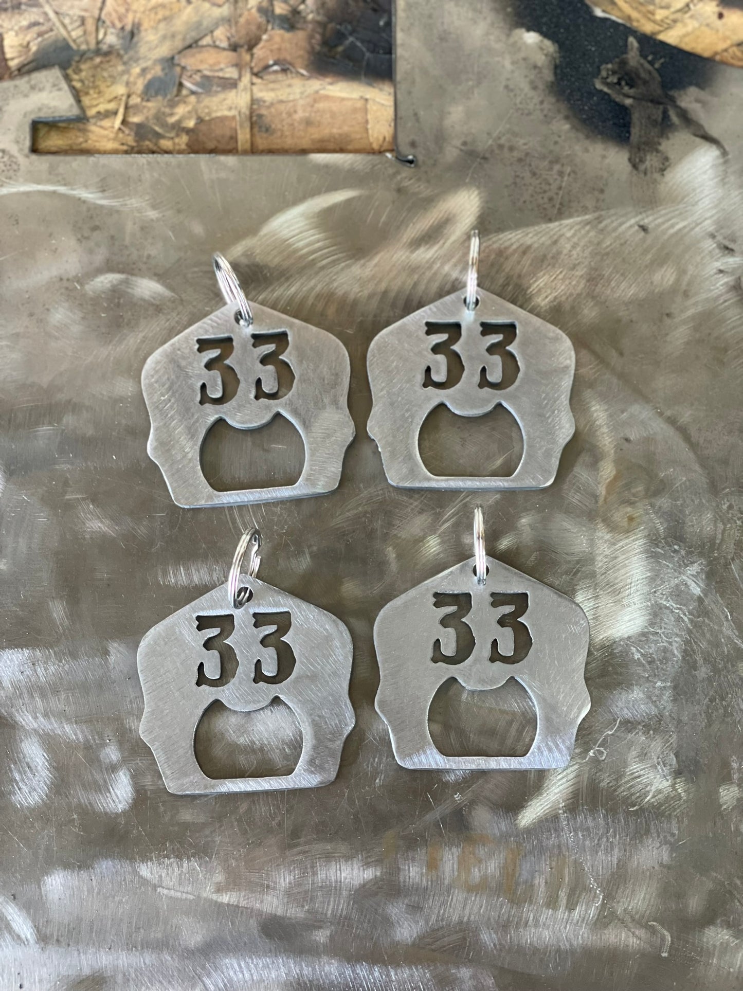 "Set of 4 raw steel firefighter helmet shield keychains with personalized unit number and built-in bottle opener, custom firefighter accessories with rugged design for keys or gear."